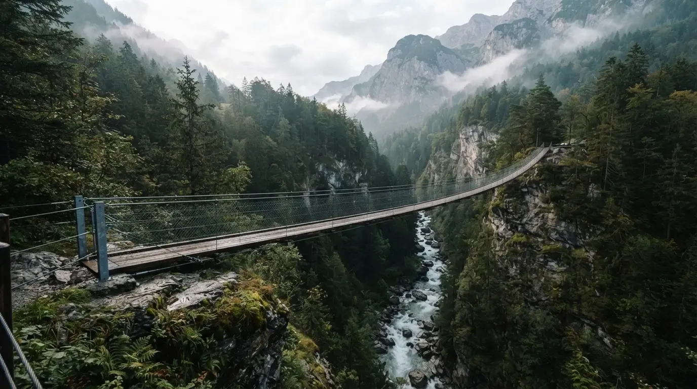 Eine Hängebrücke spannt sich über eine tiefe Schlucht, unten rauscht ein Fluss zwischen bewaldeten Felswänden.