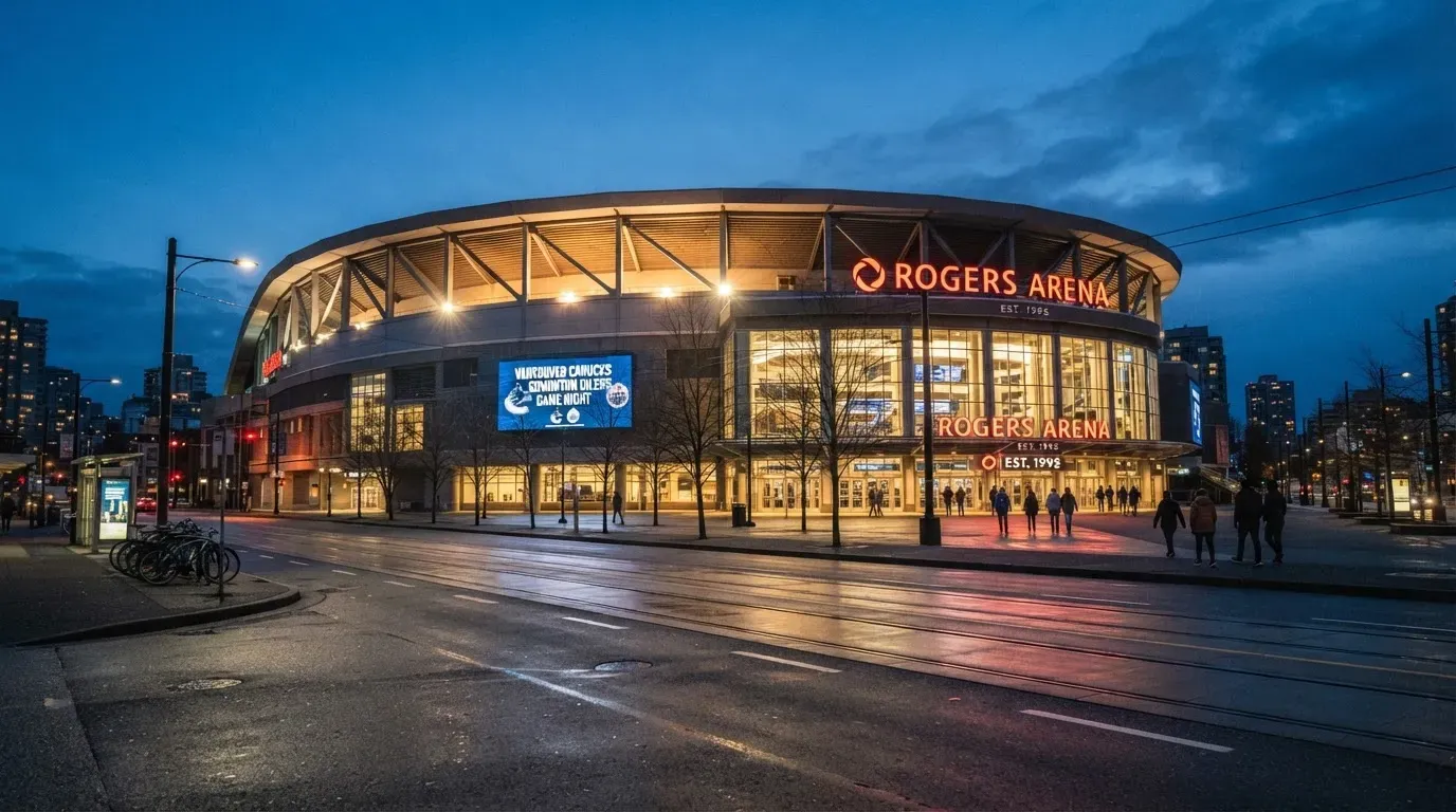 Ein grosses Eisstadion aus der Ferne gesehen, hell erleuchtet von Flutlicht in der Abenddämmerung, davor eine leere Strasse.