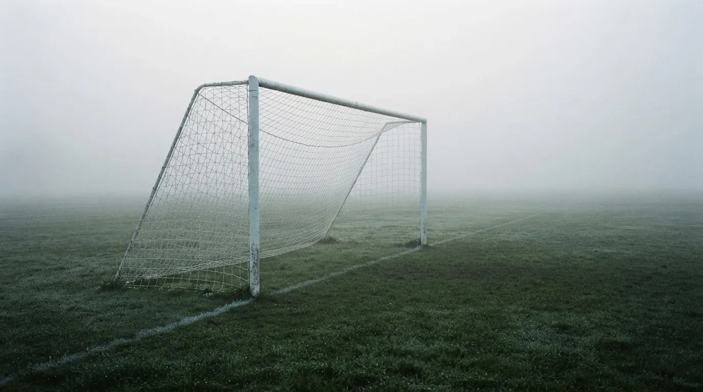 Eine Torlinie mit Netz steht am frühen Morgen im dichten Nebel auf einem Rasenplatz, die Umrisse der Pfosten verschwimmen.
