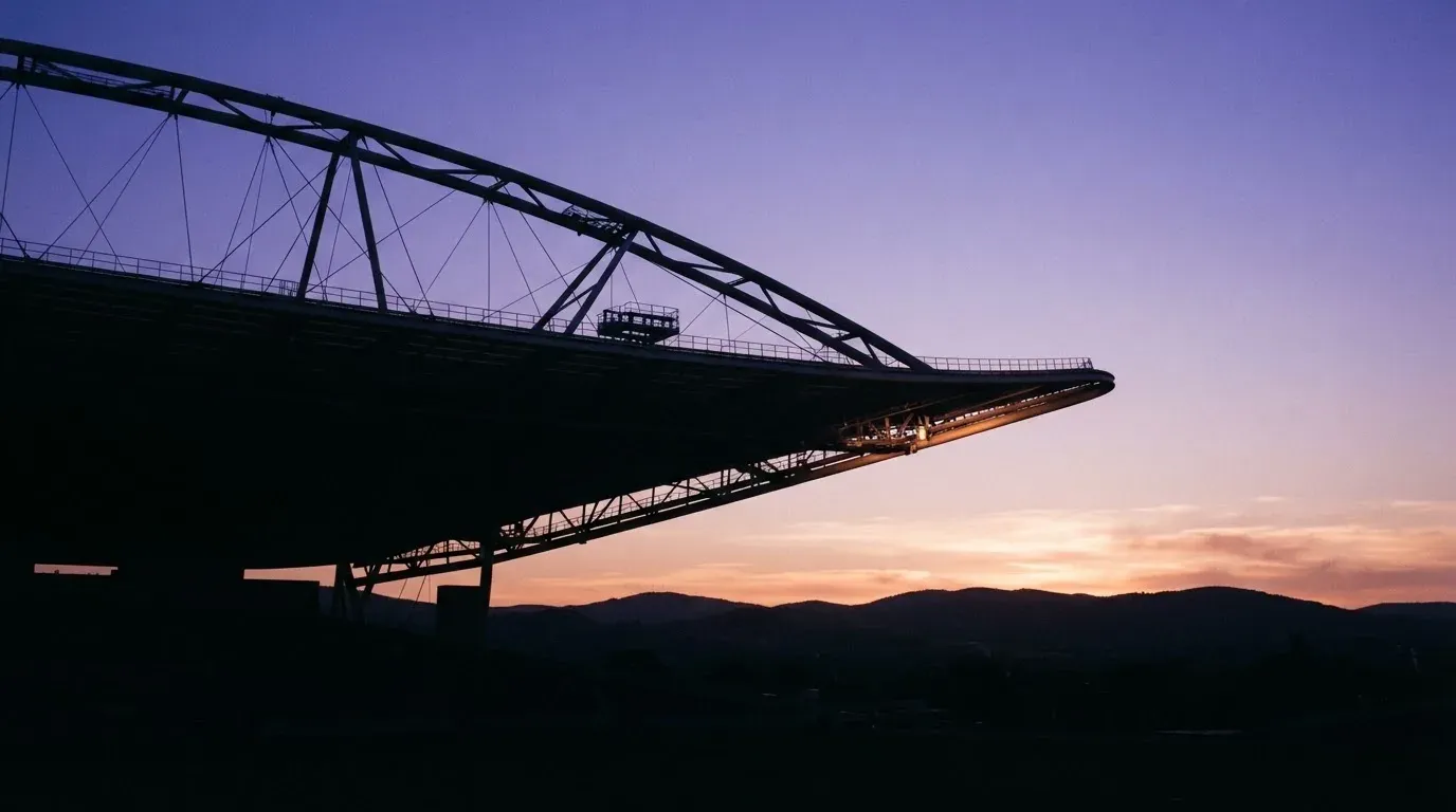 Die Silhouette eines Stadiondachs vor dem violetten Abendhimmel, dahinter eine Hügelkette.
