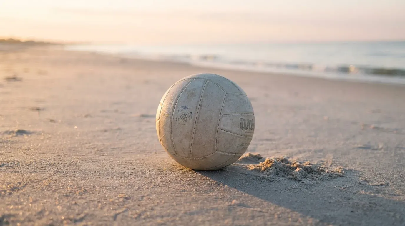 Ein Volleyball liegt auf feinem Sand an einem leeren Strand bei Sonnenaufgang.