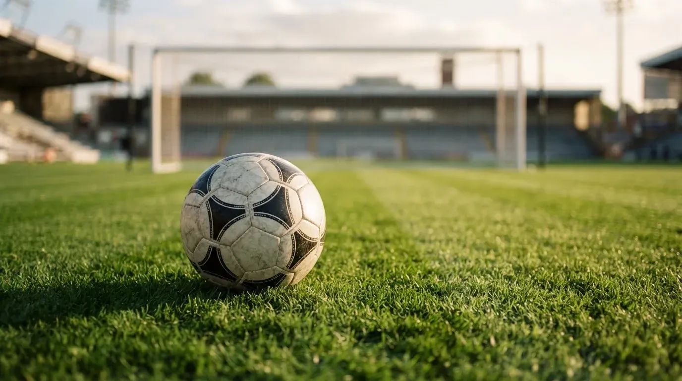 Ein Fussball auf dem Rasen aus niedriger Perspektive aufgenommen, die Torpfosten verschwimmen im Hintergrund.
