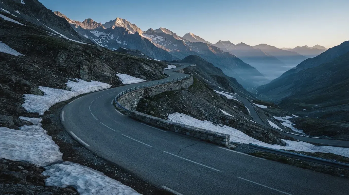Ein Bergpass in den Schweizer Alpen mit leerer Strasse und Schneeresten am Rand im ersten Frühlicht.