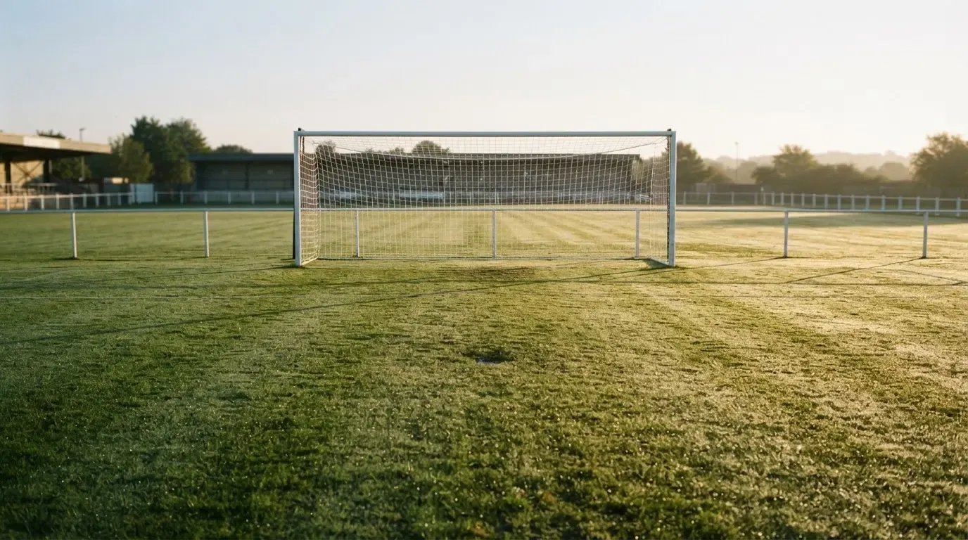 Ein Fussballtor mit Netz in der Totalen auf einem leeren Platz, Tau glänzt im Gras und die Morgensonne steht tief.