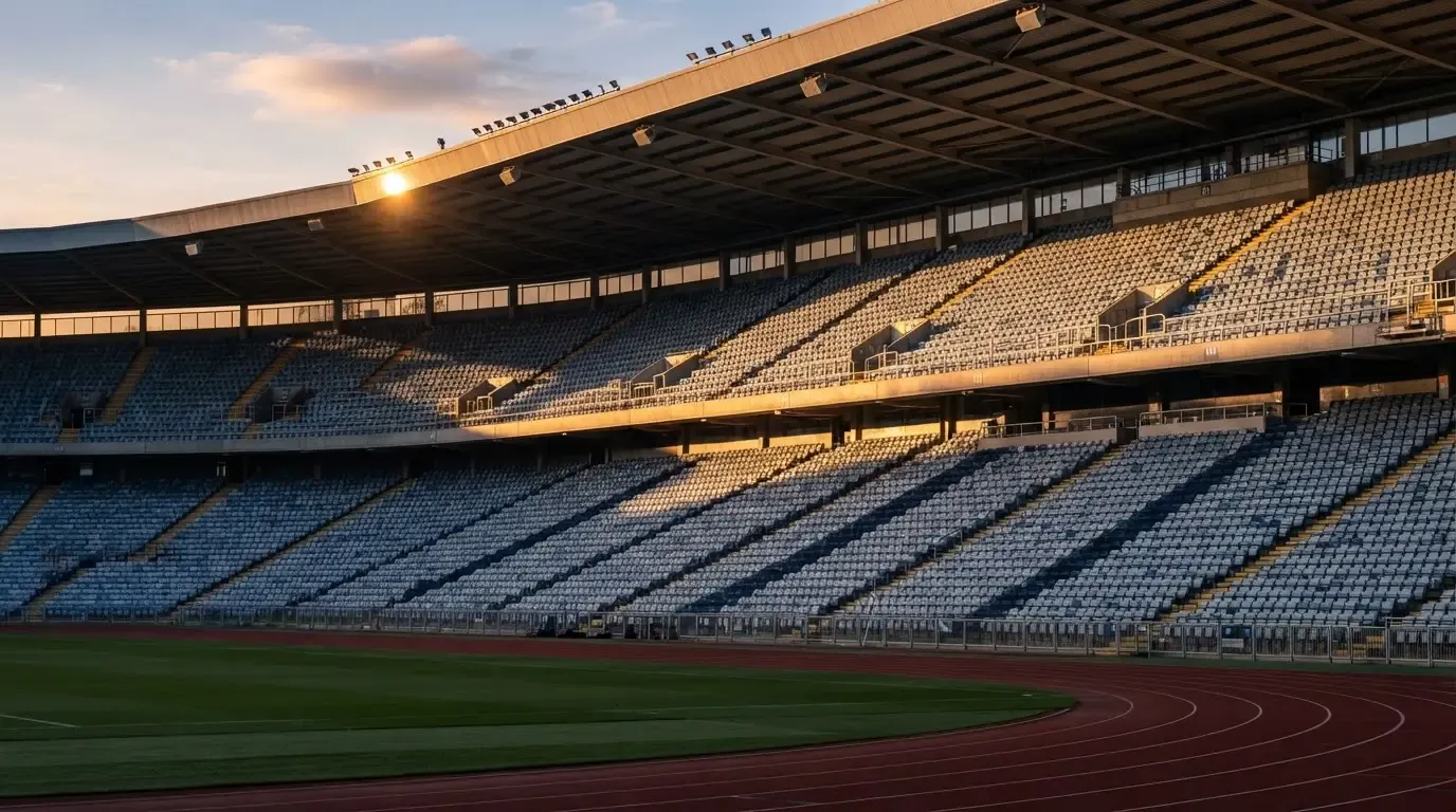 Eine leere Stadiontribüne bei Sonnenaufgang aus der Ferne, lange Schatten fallen über die Sitzreihen