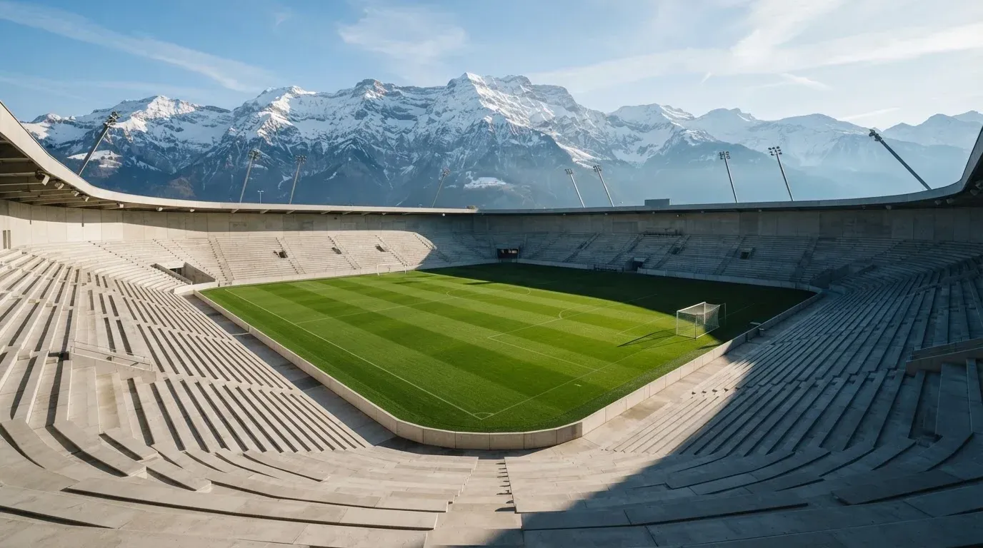 Schneebedeckte Berggipfel erheben sich im klaren Morgenlicht hinter einem leeren Stadion mit hellen Zuschauerrängen.
