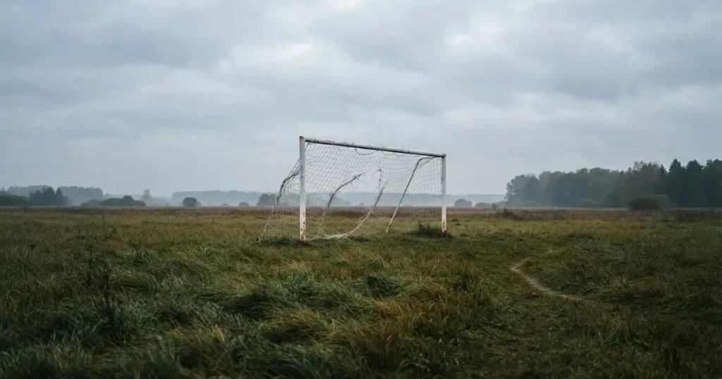 Ein Torpfosten mit Latte steht aus der Ferne vor grauem Himmel auf einer Wiese.