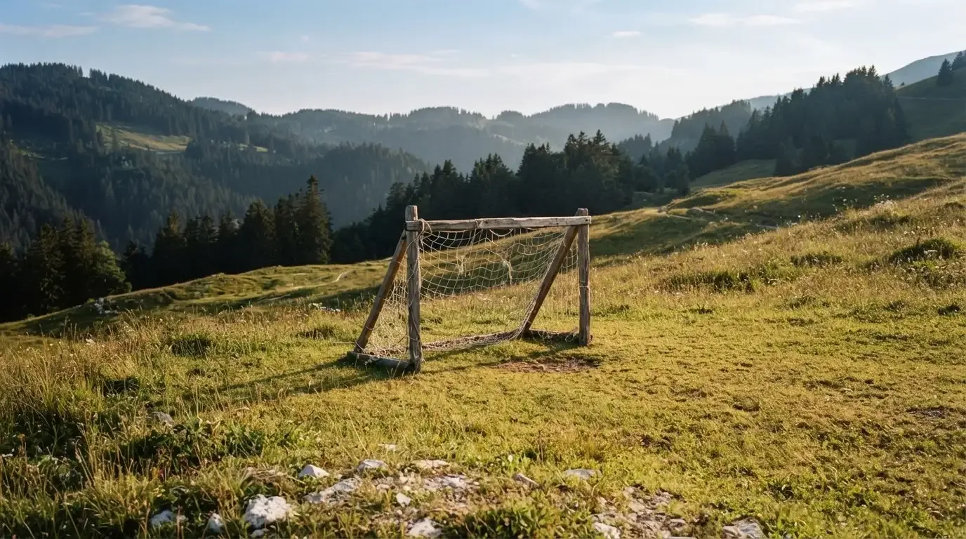 Eine Almwiese mit einem kleinen Holztor für Kinderfussball, dahinter erheben sich bewaldete Hänge im Nachmittagslicht.