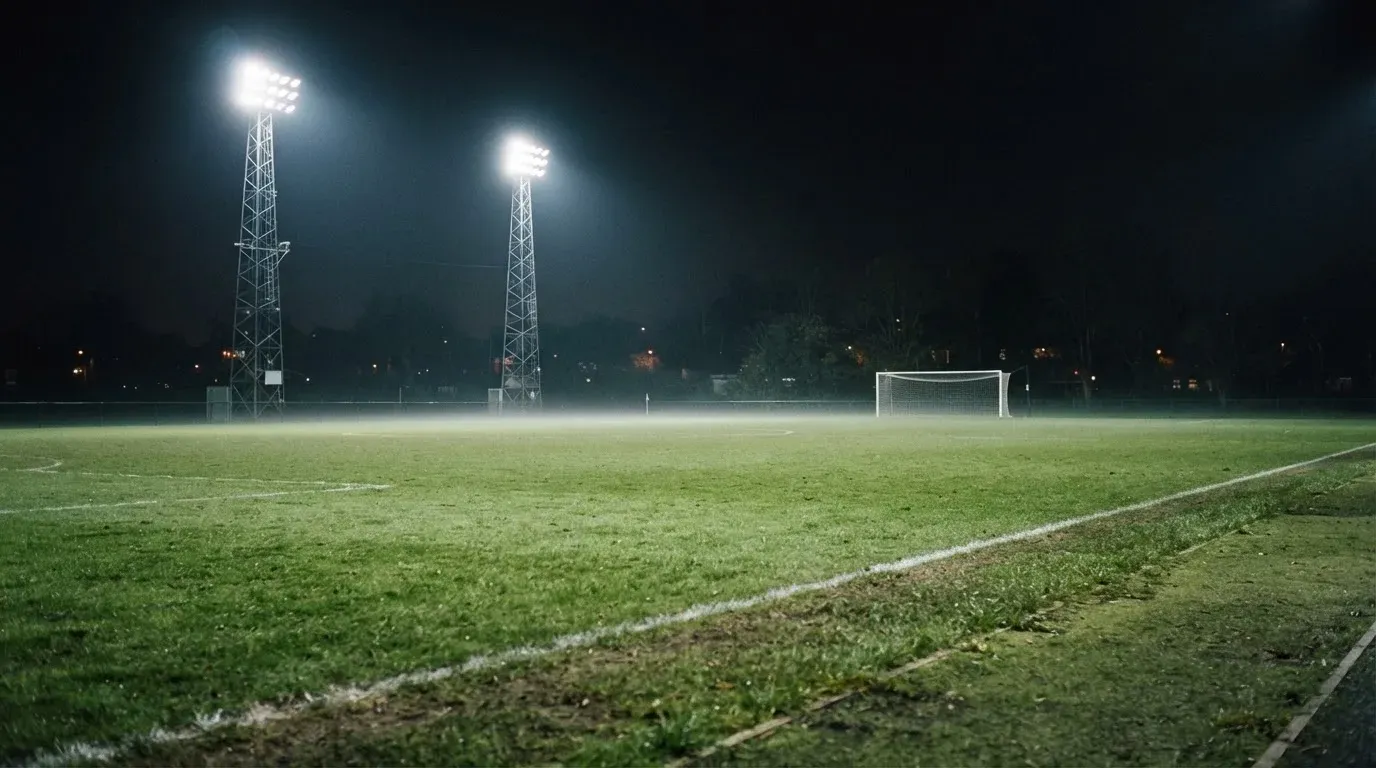 Hohe Flutlichtmasten ragen nachts über einen leeren Trainingsplatz, der Rasen glänzt im weissen Licht.