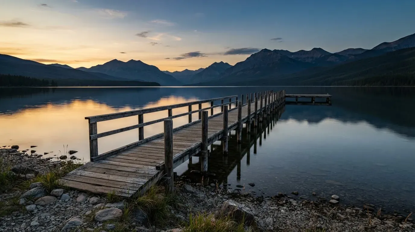 Ein leerer Holzsteg ragt am Abend in einen ruhigen Bergsee, das Wasser spiegelt den Himmel.