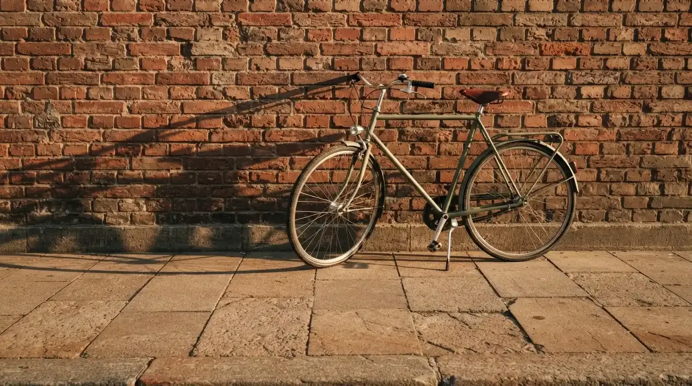 Ein Fahrrad lehnt an einer Backsteinmauer, auf dem Gehweg davor fallen lange Schatten.